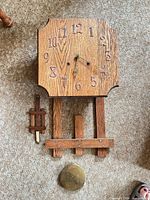 Clock body, pendulum stick, and brass bob laid out on carpet