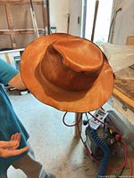 Three-quarter view of brown leather hat showing crown, brim and edge trim