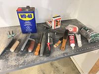 Group shot showing WD-40 can, multiple trowels, wire brush, adhesives, knife, steel wool