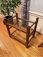 Full view of end table showing wood frame, glass top and lower shelf, casters visible