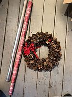 Pinecone wreath with red bow and two wrapping paper rolls on floor
