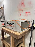 Full view of Ridgid AF3000 air filtration system on bench showing housing, grille, branding and mounting chains