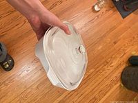 White ceramic square baking dish with clear glass lid held in hand