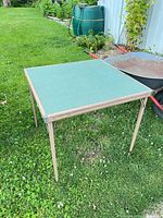 Full view of folded-out square table on lawn showing green top and beige legs