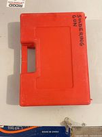 Closed red plastic case marked Soldering Gun