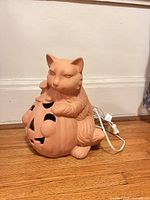 Cat sitting on jack-o-lantern ceramic figure with cord