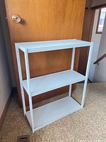 Full view of three-shelf white metal frame unit against door