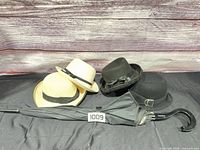group view showing two beige straw hats, black felt hat, black Chantal Thomass umbrella