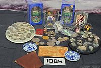 Overview of entire lot showing coins, banknote, glass mug, boxed tins, souvenir plates, wallet, ceramic dishes, frames, charms