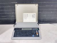 Typewriter open with manual and cord visible