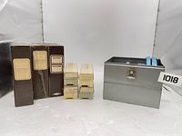 Group shot: three slide boxes, six plastic trays stacked, grey metal case with reel, lot overview