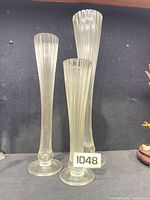 Three ribbed clear glass bud vases on shelf