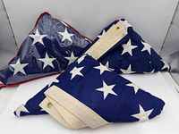 Three folded American flags, one in clear vinyl display case, showing embroidered stars and headers