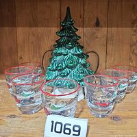 Front view of seven sleigh scene shot glasses arranged around green ceramic Christmas tree lamp