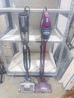 Full view of both Shark stick vacuums standing side by side on shelving