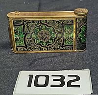 front view of brass enamel camera-style compact showing green and black arabesque design
