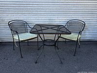 front view of square wrought iron patio table with two matching chairs and cushions