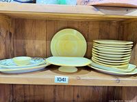 Shelf with stacked yellow plates, cake stand, platters and bowl