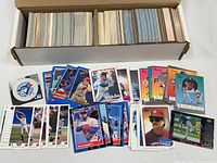 Open long box packed with unsorted baseball cards and sample cards spread out, including Blue Jays sticker