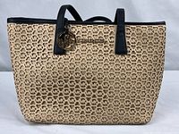 Front view of beige MK laser-cut tote with black handles and gold charm