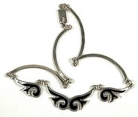 Full view of articulated sterling silver necklace showing curved bar links and three black enamel wing motifs