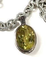 Close view of pendant showing oval faceted faux olivine stone, bezel setting, textured bail and chain detail