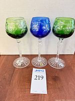 Front view of three lead crystal wine glasses, two green one blue, showing full design and labels