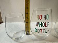 Plain clear stemless glass and XL clear glass with HO HO WHOLE BOTTLE print beside measuring tape