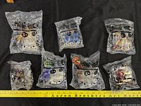 Six sealed Justice League kids meal figures laid out with ruler for scale