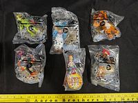 Six sealed Jack in the Box kids meal toy bags laid on black fabric with yellow ruler for scale
