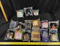 Sixteen sealed McDonald's Happy Meal toys displayed with measuring sticks for scale