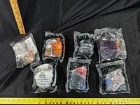 Seven individually bagged Chicken Little Happy Meal toys displayed on black background with measuring rulers