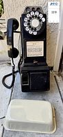 Full view of black rotary wall pay phone with handset and coin compartment