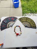 Lot overview: two folding fans and ceramic bead necklace on table