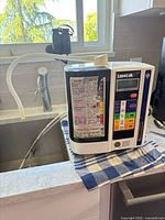 Angled front view of water ionizer on countertop with flexible hose attached