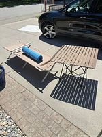 Full view of slatted table, camping cot and rolled yoga mat outdoors