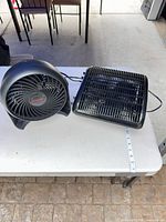 Honeywell circular fan and generic square fan on table with power cords visible