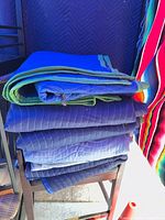 Stack of folded blue moving blankets with green trim on chair