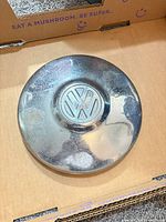Front view of Volkswagen chrome hubcap showing VW emblem and surface wear