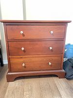 Front view of three-drawer cherry dresser with silver knobs