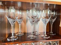 Six clear crystal red wine glasses with sculpted stems displayed on shelf
