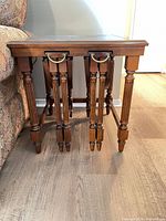 Set of three walnut-finish wooden nesting tables with brass drop handles shown nested together beside sofa