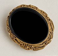 Front view of brooch showing gold filigree and black cabochon