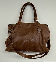 Front view of brown leather Roots bag showing handles and detachable strap