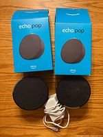 Two Echo Pop speakers, two retail boxes, and power adapter on wooden surface