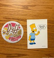 Front view of Duff Beer coaster and Bart Simpson postcard
