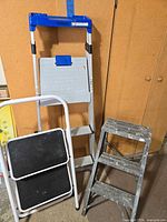 All three ladders grouped: Cosco ladder, white 2-step stool, grey 3-step stool