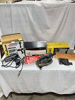 Group shot of sander, heat gun with box, mitre box, sanding pads, accessories