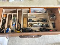 Drawer view showing assorted blades, scrapers, PTFE tape, bracket, drill bit holder, caps, knobs and fasteners