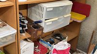 Shelving unit showing white plastic two-drawer cabinet, box of sanding supplies and surrounding items
